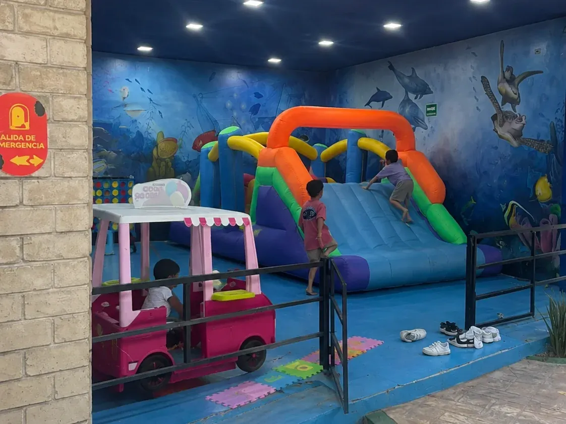 Covered playground with an inflatable and colorful play equipment, with an ocean mural on the wall